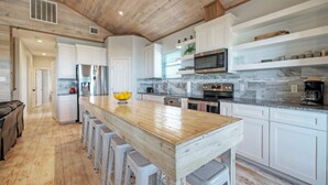 Une cuisine moderne avec des meubles blancs, un îlot central en bois doté de tabourets, des appareils électroménagers en acier inoxydable et un pare-feu en marbre.