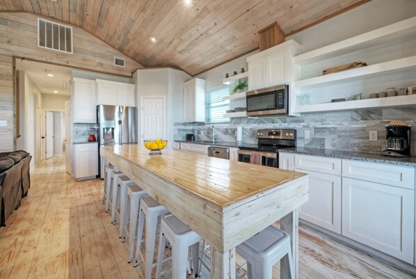A modern kitchen with white cabinets, a wooden island with bar stools, stainless steel appliances, and a marble backsplash.