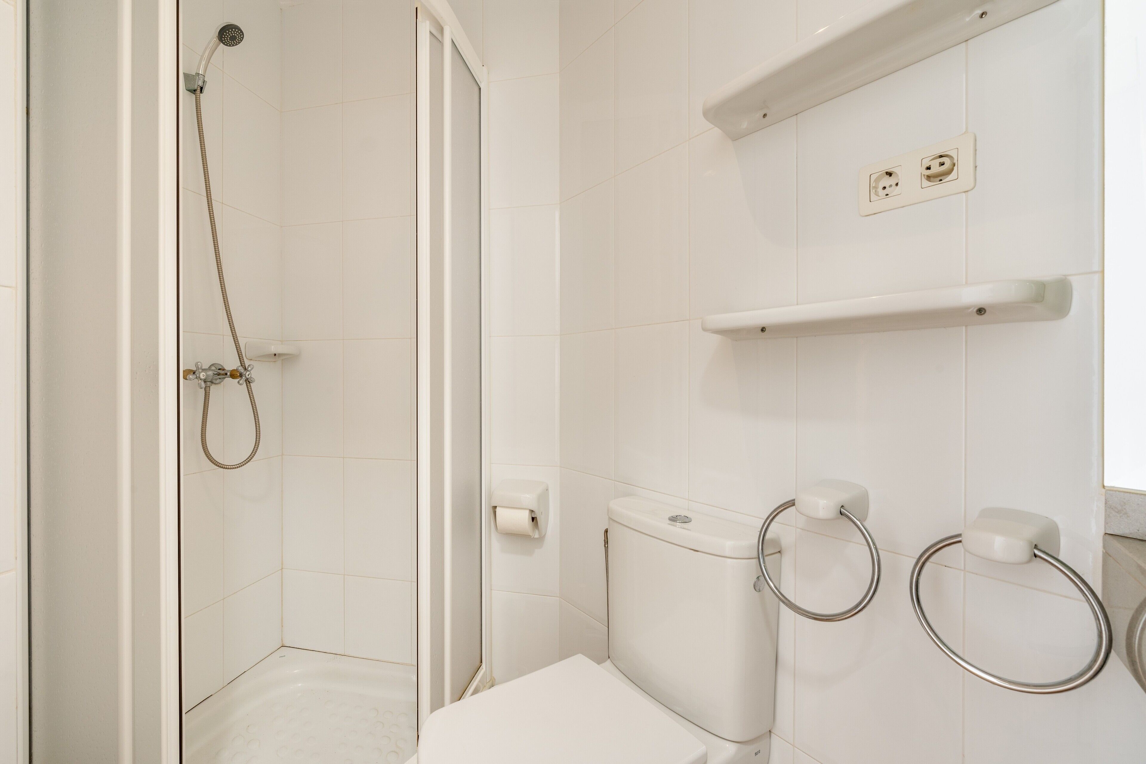 A bathroom with a shower, toilet, and towel rings.