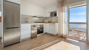 Una cucina moderna con mobili bianchi, elettrodomestici in acciaio inossidabile e vista mare da un balcone.