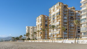 Un hotel a più piani con balconi, situato vicino a una spiaggia con palme.