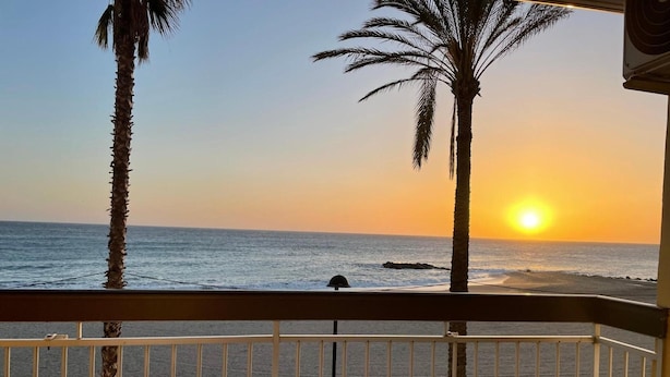 Un balcone con sedie in vimini, una ringhiera e vista sull'oceano al tramonto.