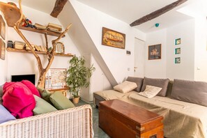 Ein gemütliches Wohnzimmer mit einer Couch, einem Holztisch, einem Korbstuhl, einem Bücherregal und einer großen Pflanze.