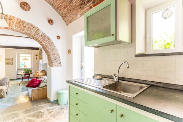 A kitchen with a stone archway, green cabinets, a stainless steel sink, and a window with a view.