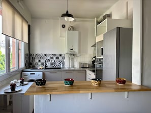 Una cocina moderna con encimera de madera, horno integrado, refrigerador y ventana con persianas.