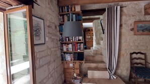 A rustic room with a bookshelf, a chair, and a staircase leading to another level. - Abbaye Cottage
Charming House in the Heart of Fontevraud-Private Garden-Jacuzzi (Fontevraud-l'Abbaye)