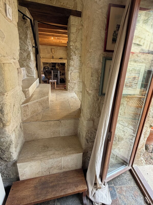 A stone staircase leading to a room with a fireplace, a wooden bench, and a view through a glass door.