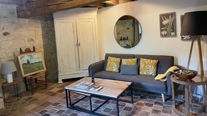 A cozy living room with a wooden ceiling, a stone wall, a sofa with patterned cushions, a coffee table, and a mirror on the wall. - Abbaye Cottage
Charming House in the Heart of Fontevraud-Private Garden-Jacuzzi (Fontevraud-l'Abbaye)