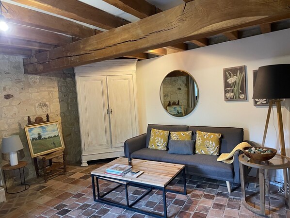 A cozy living room with a wooden ceiling, a stone wall, a sofa with patterned cushions, a coffee table, and a mirror on the wall. - Abbaye Cottage
Charming House in the Heart of Fontevraud-Private Garden-Jacuzzi (Fontevraud-l'Abbaye)