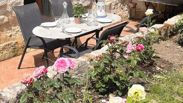 A stone building with a table set for two, surrounded by a garden with roses. - Abbaye Cottage
Charming House in the Heart of Fontevraud-Private Garden-Jacuzzi (Fontevraud-l'Abbaye)