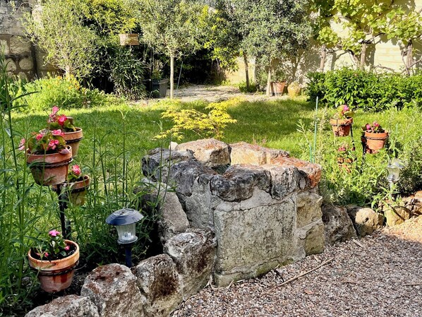 Un jardín con plantas en macetas, un muro de piedra y un farol.