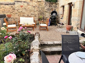 A patio with stone walls, outdoor furniture, a grill, and potted plants.
