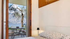 Un dormitorio con cama, mesita de noche, lámpara y vistas a un balcón con mesa y sillas.
