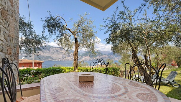 Una mesa redonda con suelo de mosaico, sillas para exteriores y vistas a montañas y una masa de agua.