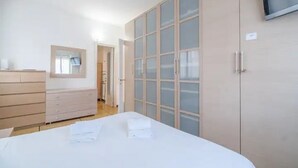 Une chambre à coucher avec un lit, une commode, une armoire et un téléviseur fixé au mur.