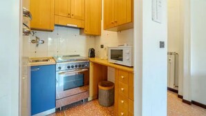 Une cuisine de taille réduite, dotée de meubles en bois, d’une cuisinière, d’un four à micro-ondes et d’une poubelle.