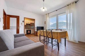 Una sala de estar con sofá, mesa de comedor con sillas, televisor y cocina al fondo.