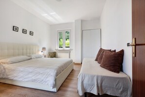 Une chambre avec un grand lit, un plus petit lit, une fenêtre, un radiateur et une porte.