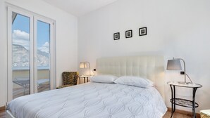 A bedroom with a bed, two bedside tables, a chair, and a view of the outdoors.