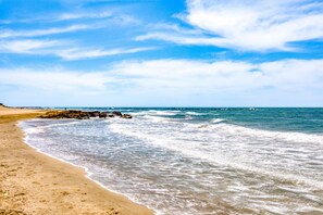 A beach with waves, a clear sky, and a rocky outcrop.