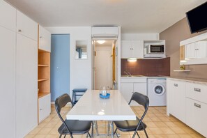 A compact kitchen with a microwave, washing machine, and a dining area with chairs.
