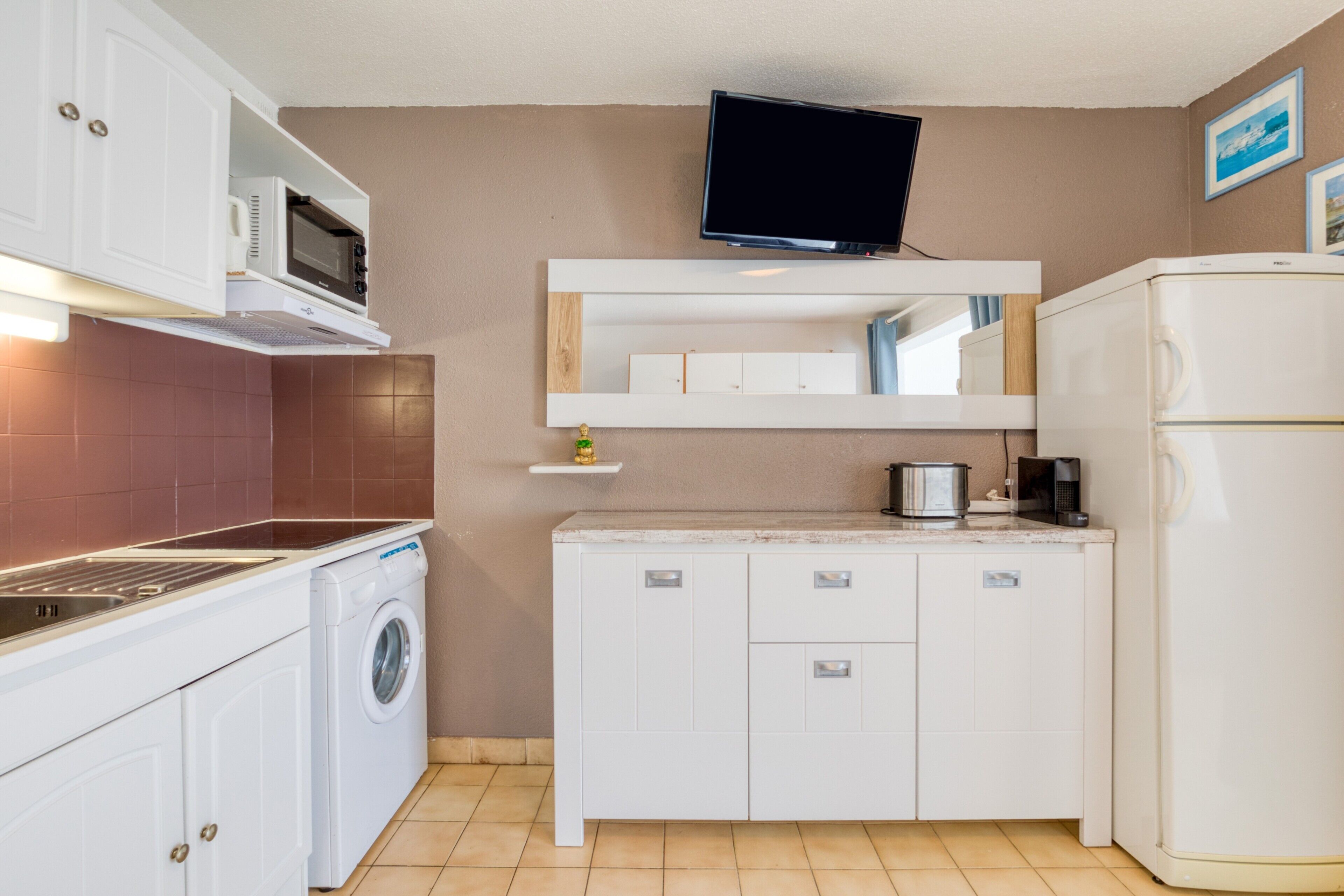 Een kleine keuken met een wasmachine, magnetron en een flatscreen televisie bevestigd boven het aanrecht.