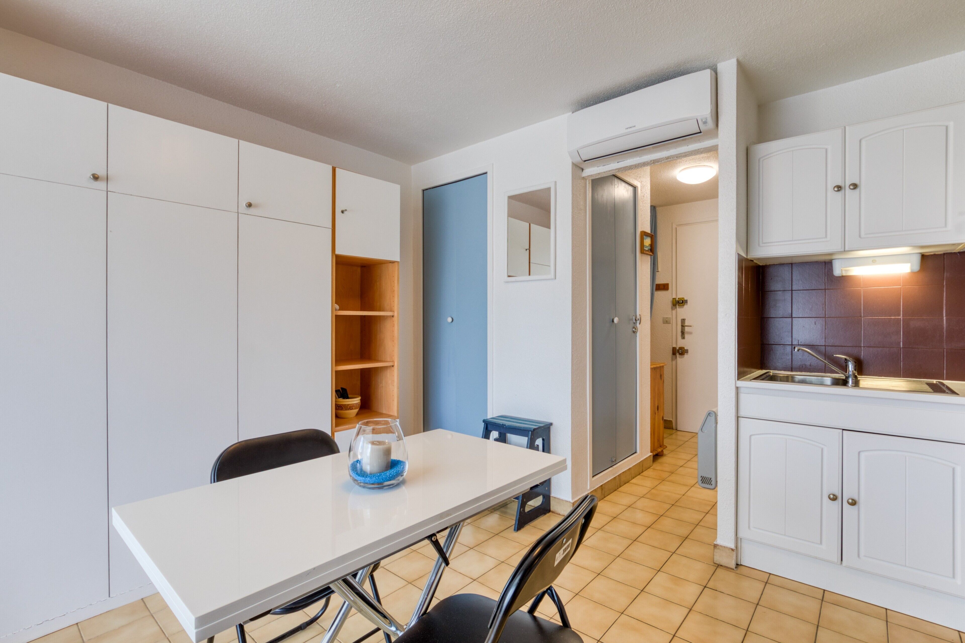 Una cucina compatta con mobili bianchi, una porta blu e un pavimento piastrellato.
