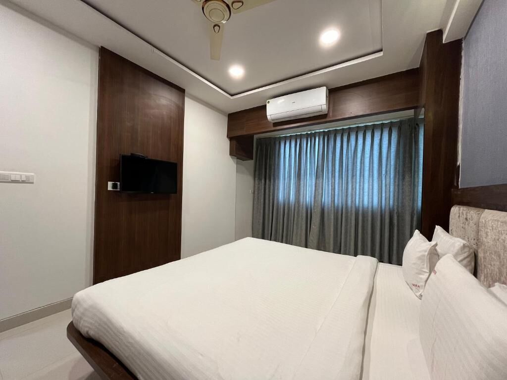 Habitación de hotel con una cama, un televisor de pantalla plana montado en la pared, un aire acondicionado y una ventana con cortinas.