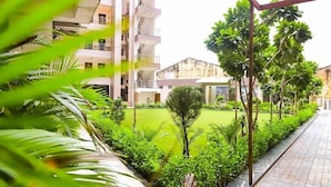 Un edificio residenziale con numerosi balconi, un giardino curato e ricco di piante e un vialetto lastricato.