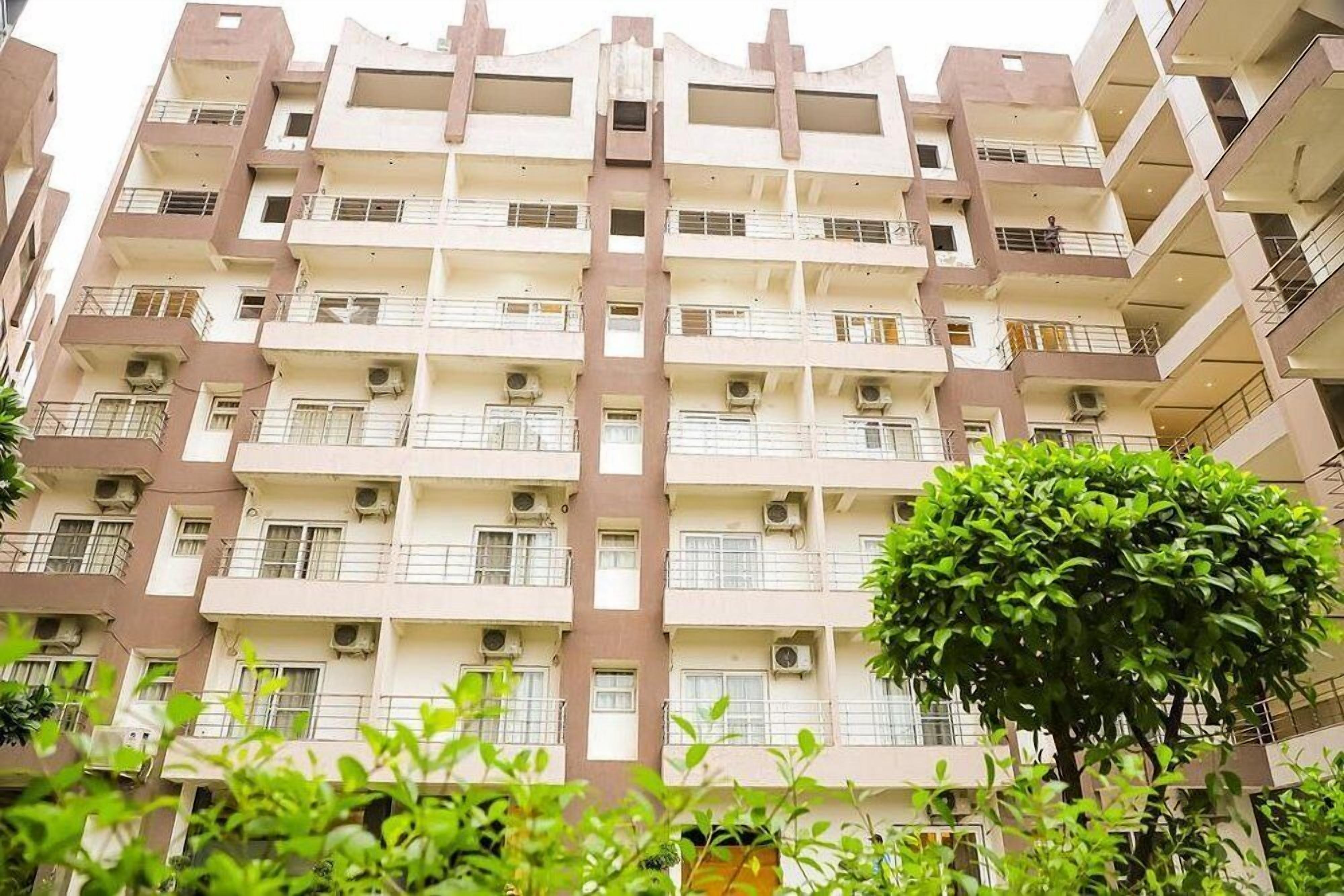 A multi-story residential building with balconies, air conditioning units, and a tree in the foreground.