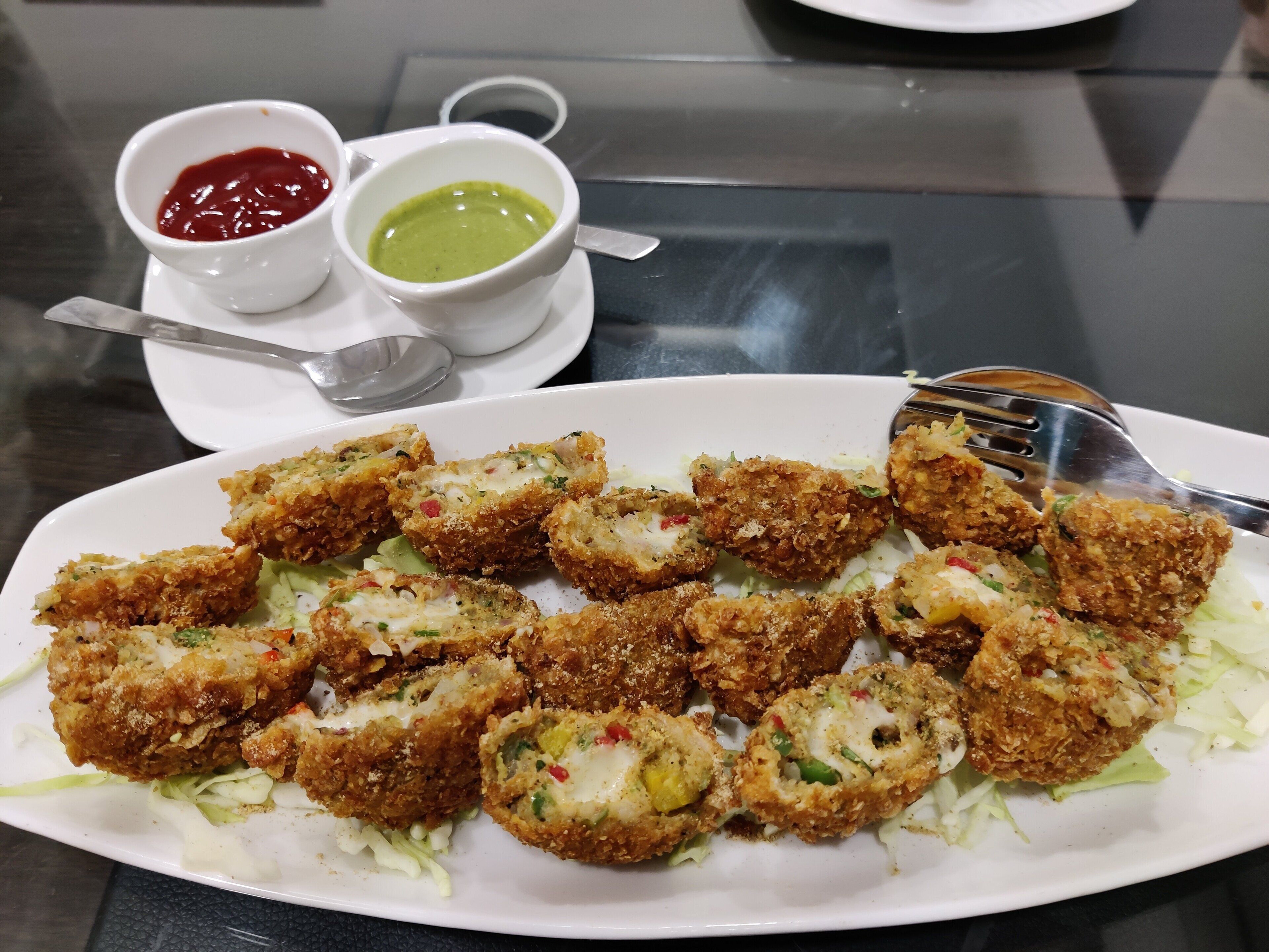 Een bord met gepaneerde en gebakken snacks, mogelijk kroketten, geserveerd op een wit bord met een portie geraspte sla.