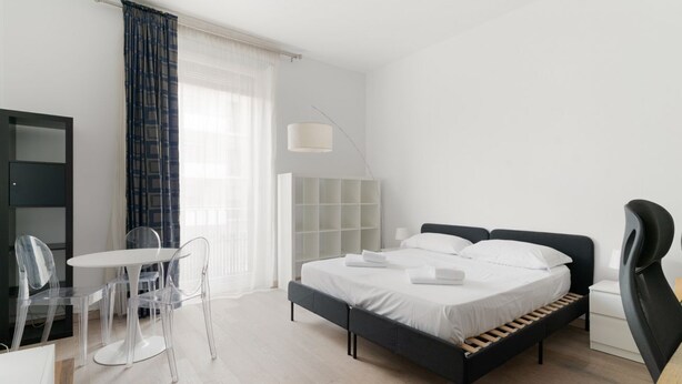 Een moderne hotelkamer met een bed, een bureau met stoel, een lamp en een kledingkast.