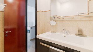Een moderne badkamer met een grote spiegel, een witte wastafel en een rode deur.