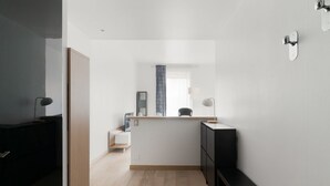 Een moderne, minimalistische kamer met een houten vloer, een zwart tv-meubel, een klein wit bureau en een spiegel aan de muur.