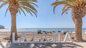 A beachside view with palm trees and a sign spelling 'LAJIA'. - Chabela's Penthouse Apartment with Sea Views, Jacuzzi, and Air Conditioning (La Lajita)