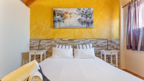 A hotel room with a large bed, two bedside tables, a painting on the wall, and a window with curtains. - Chabela's Penthouse Apartment with Sea Views, Jacuzzi, and Air Conditioning (La Lajita)
