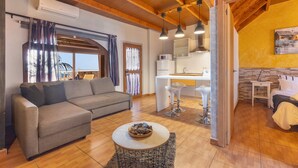 A living room with a sofa, a round coffee table, and a kitchen area with a refrigerator and sink. - Chabela's Penthouse Apartment with Sea Views, Jacuzzi, and Air Conditioning (La Lajita)