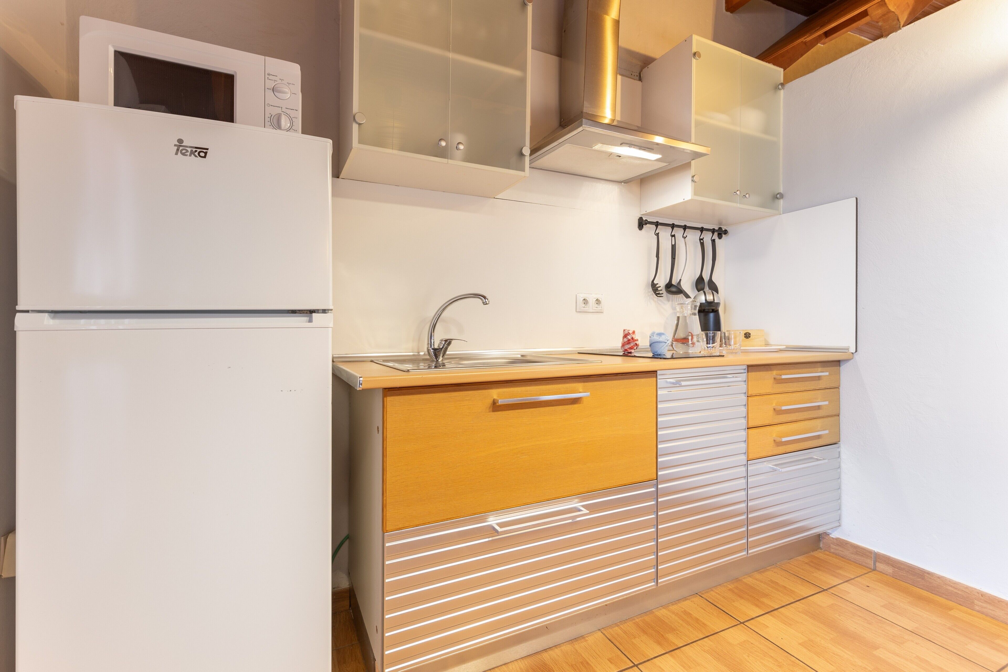 Eine Küche mit einem weißen Kühlschrank, Holzschränken, einer Edelstahlspüle und einem Küchenutensilienhalter.