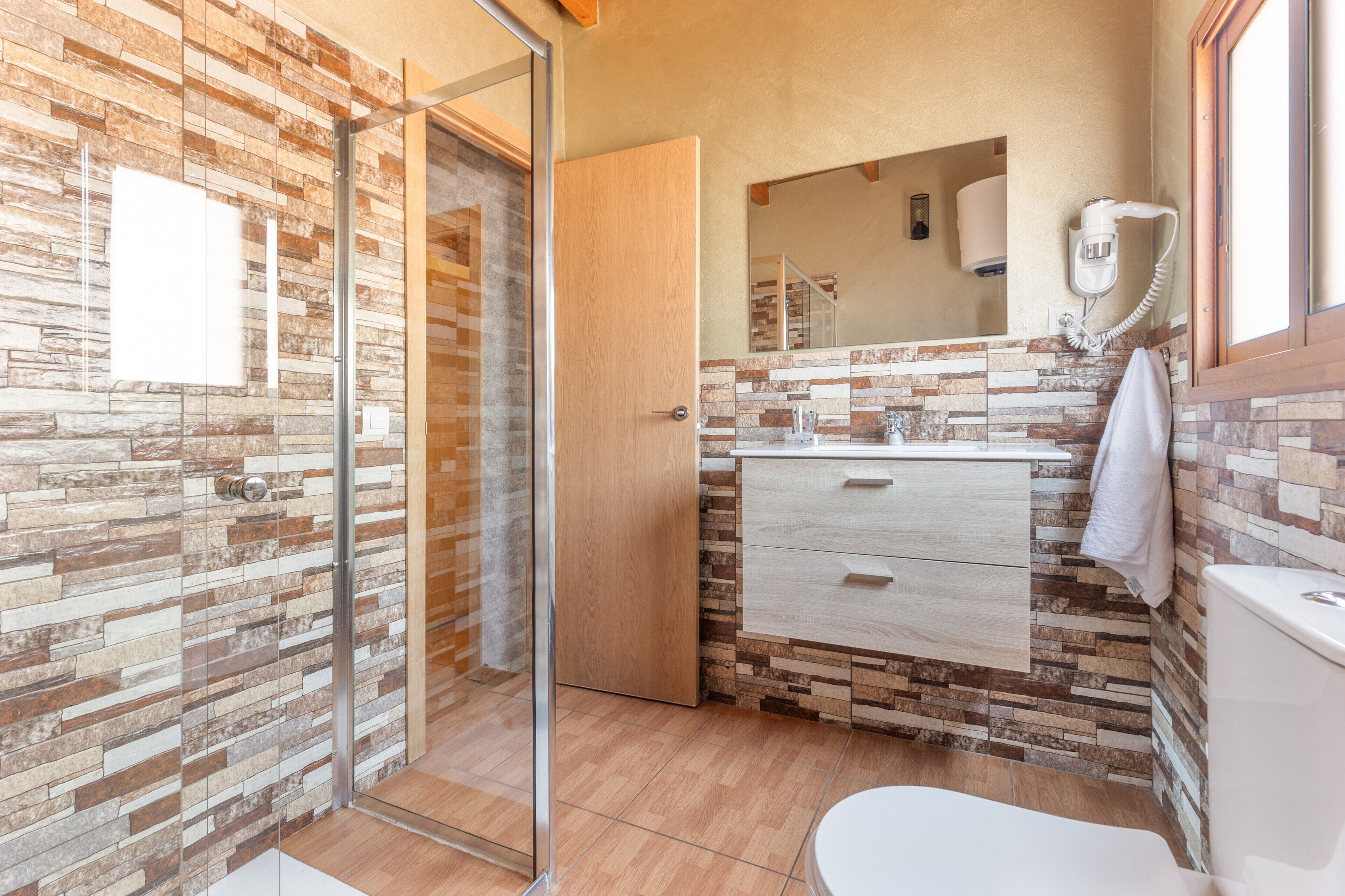 A bathroom with a glass shower door, a wooden vanity, a toilet, and a towel hanging on the wall.