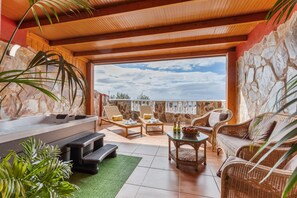 A sunlit outdoor lounge area with stone walls, a hot tub, wicker furniture, and a view of the sky. - Chabela's Penthouse Apartment with Sea Views, Jacuzzi, and Air Conditioning (La Lajita)