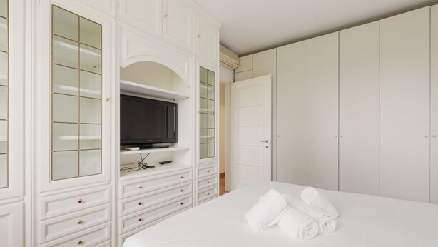 A bedroom with a bed, a television on a stand, a wardrobe, and a door.