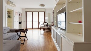 A living room with a sofa, a dining table with chairs, a TV, and built-in shelving.