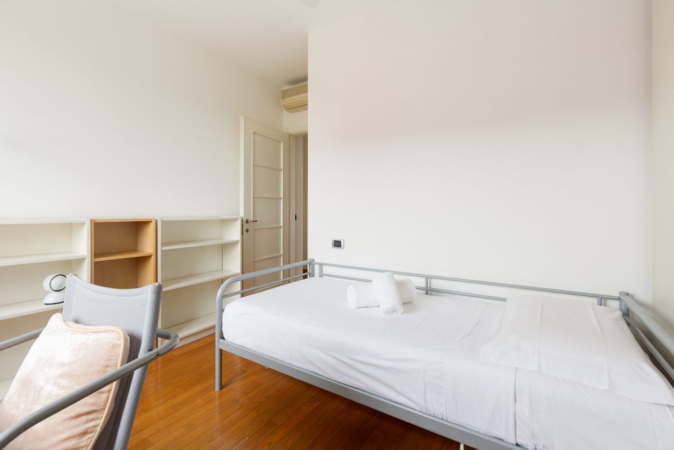 Una habitación de hospital con una cama individual, una mesita de noche, una silla y un estante de madera.