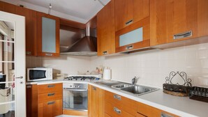A kitchen with wooden cabinets, a microwave, stove, sink, and a basket on the countertop.
