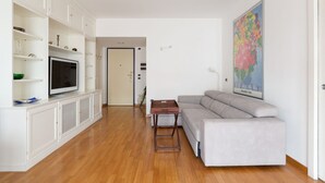 A living room with a sofa, TV, white cabinets, and a painting.