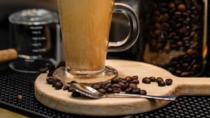 En kopp kaffe på en underlägg, med kaffebönor och en kaffekvarn i bakgrunden.