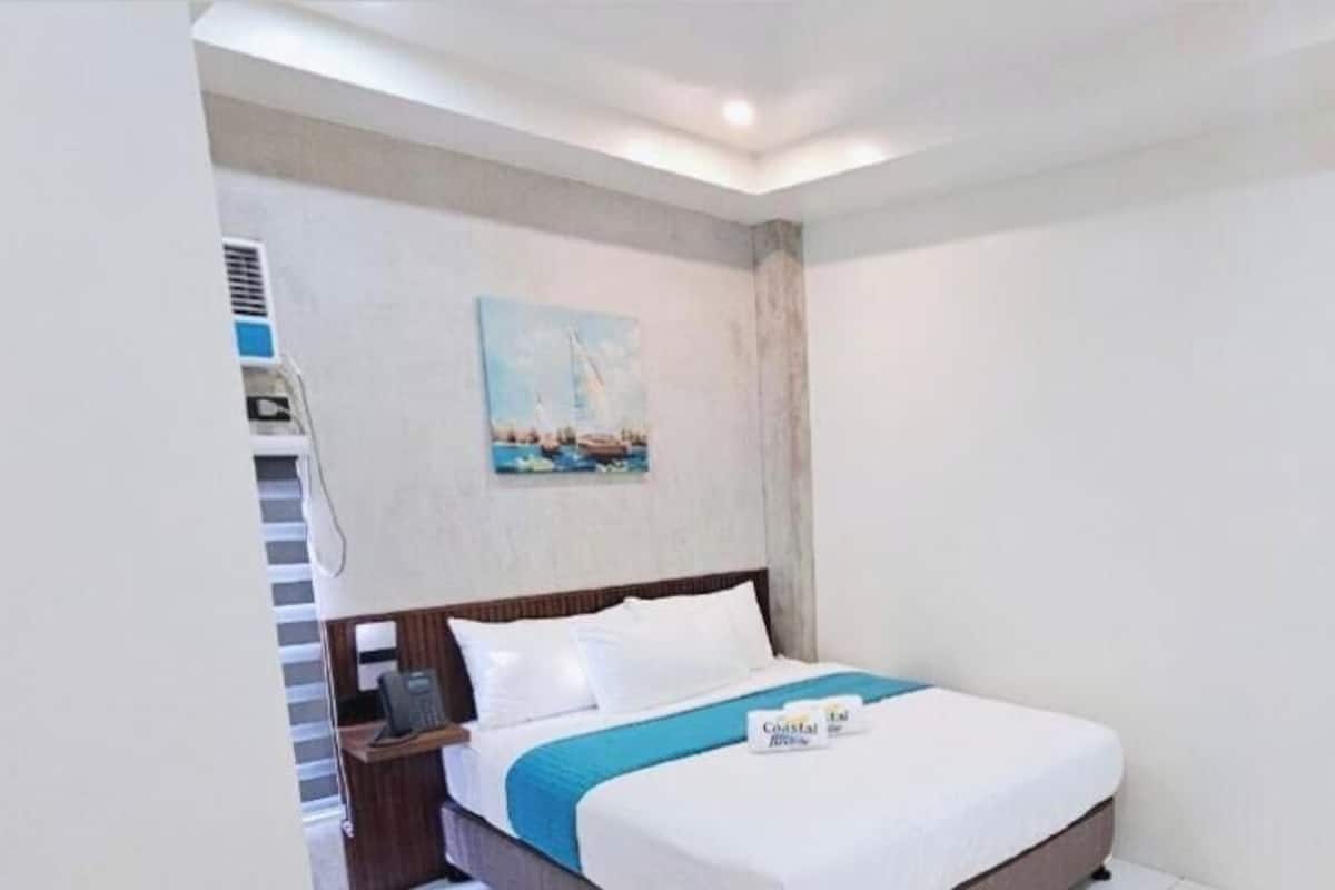 A hotel room with a bed, a nightstand, a painting on the wall, and a window.