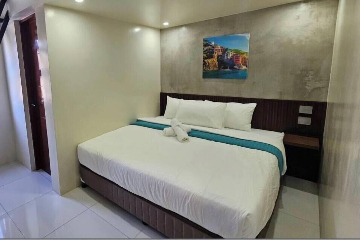A hotel room with a large bed, a headboard, a painting on the wall, and a door.