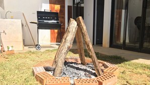 A backyard with a brick fire pit surrounded by bricks, a grill, and a wheelbarrow.
