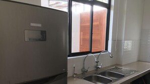 A kitchen with a stainless steel refrigerator, a double sink, and a window with blinds.